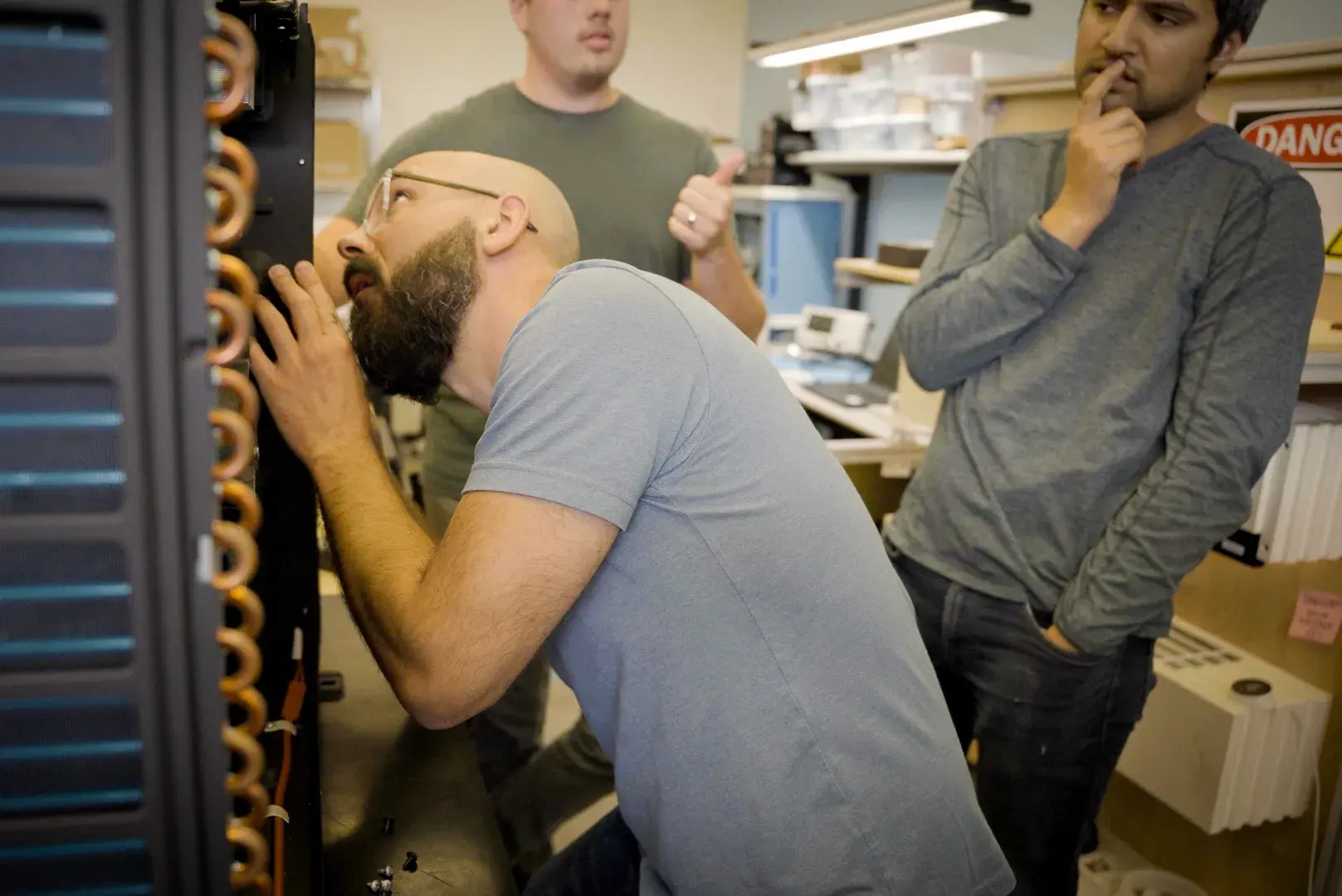 A trio of engineers looking carefully at a Quilt outdoor unit in an engineering lab.