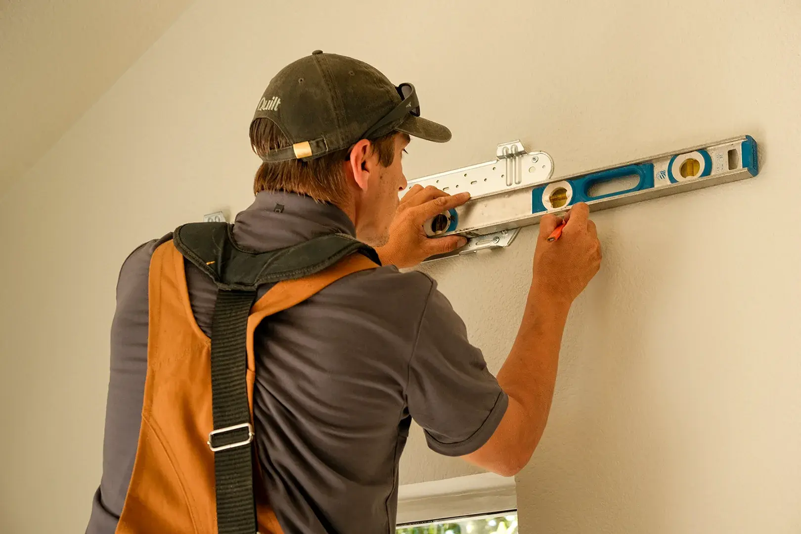 An HVAC installer using a level to carefully position a Quilt indoor unit on a beige wall.